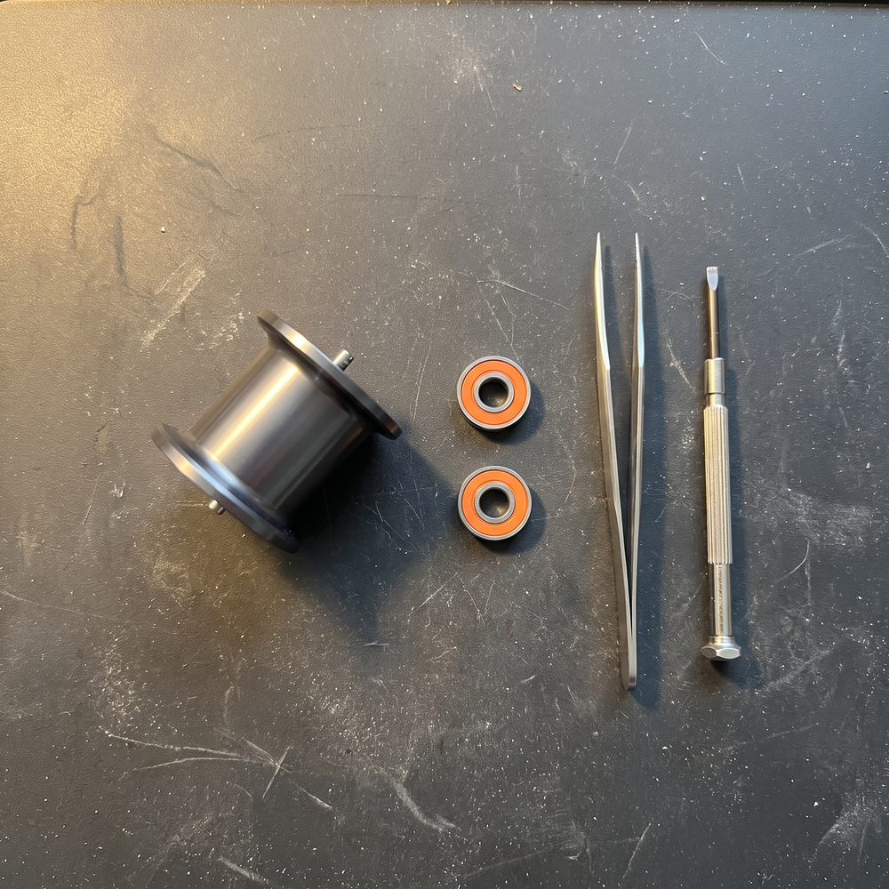 Two sealed Edge spool bearings next to a baitcaster spool and tweezers on the workbench